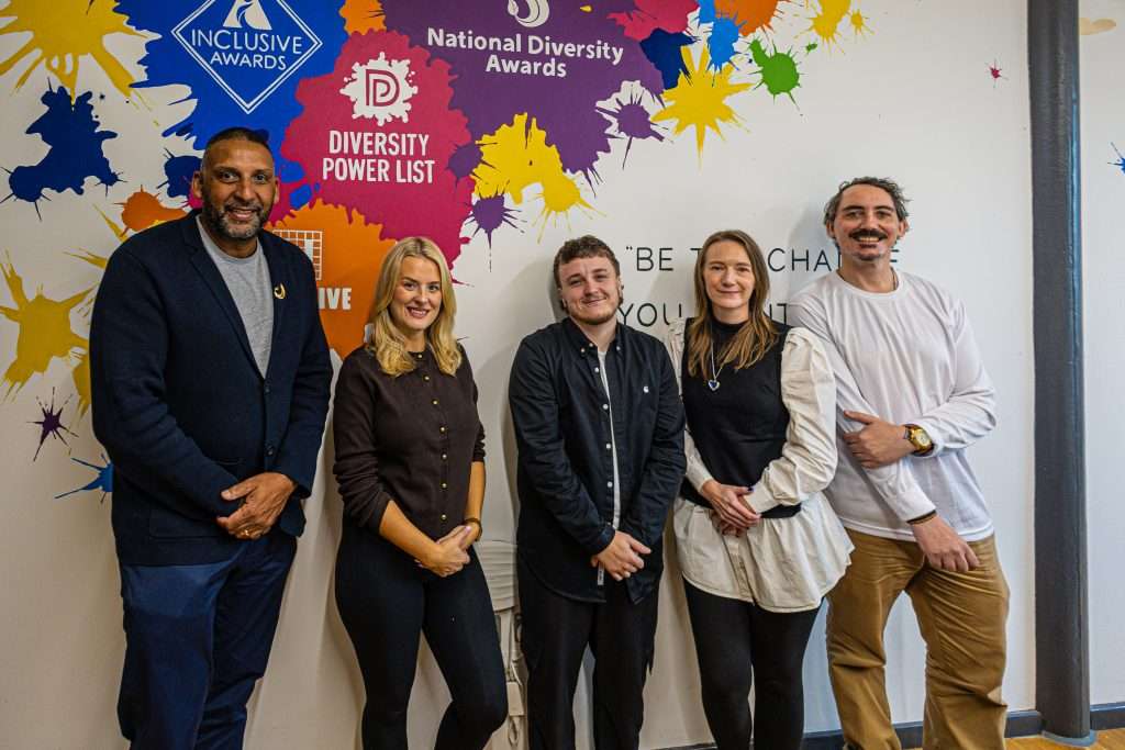 Inclusive Companies team of 5 standing against a branded wall